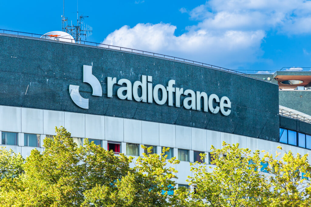 Façade extérieure du bâtiment de la Maison de la Radio avec le logo officiel de Radio France sous un ciel bleu.